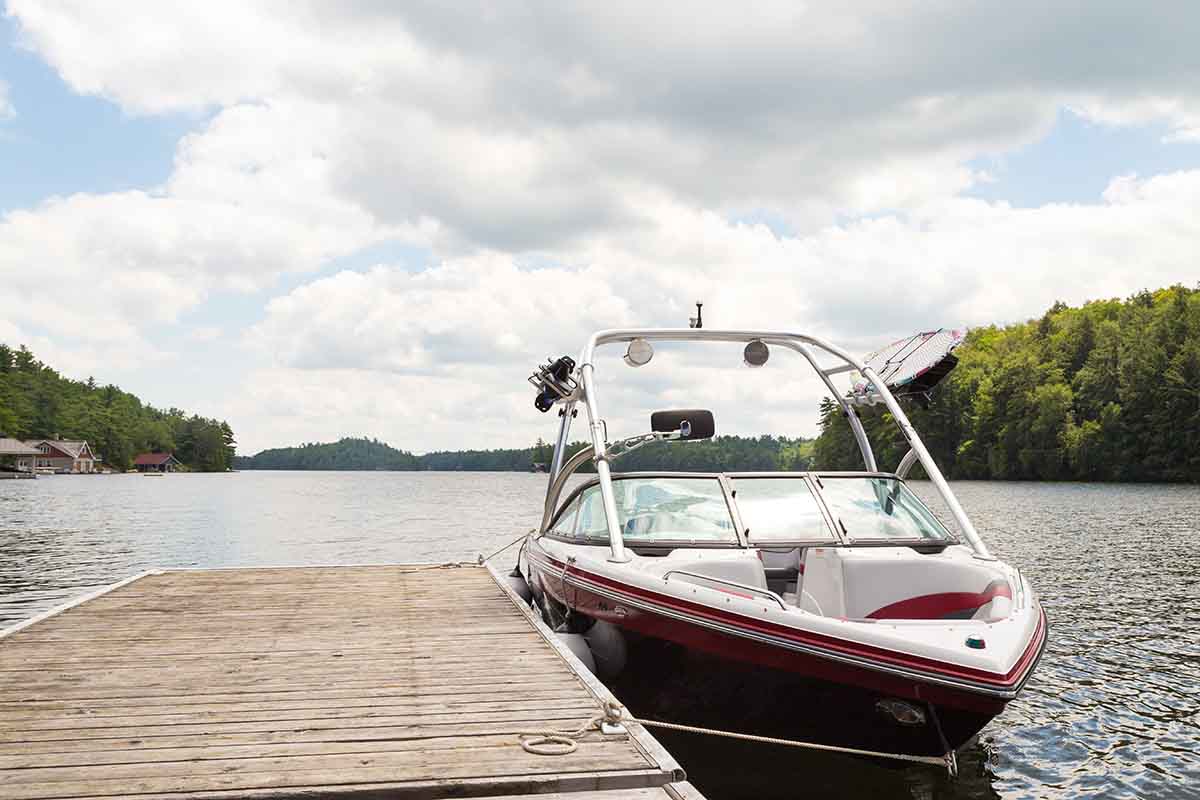 A wakeboard boat at a wooden dock in the Muskokas on a sunny day.